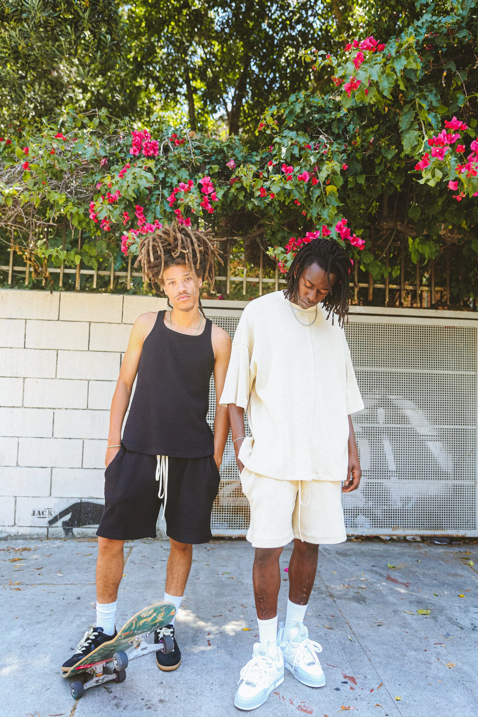 Two Cannon Mitchel models standing near a skateboard in summer light.
