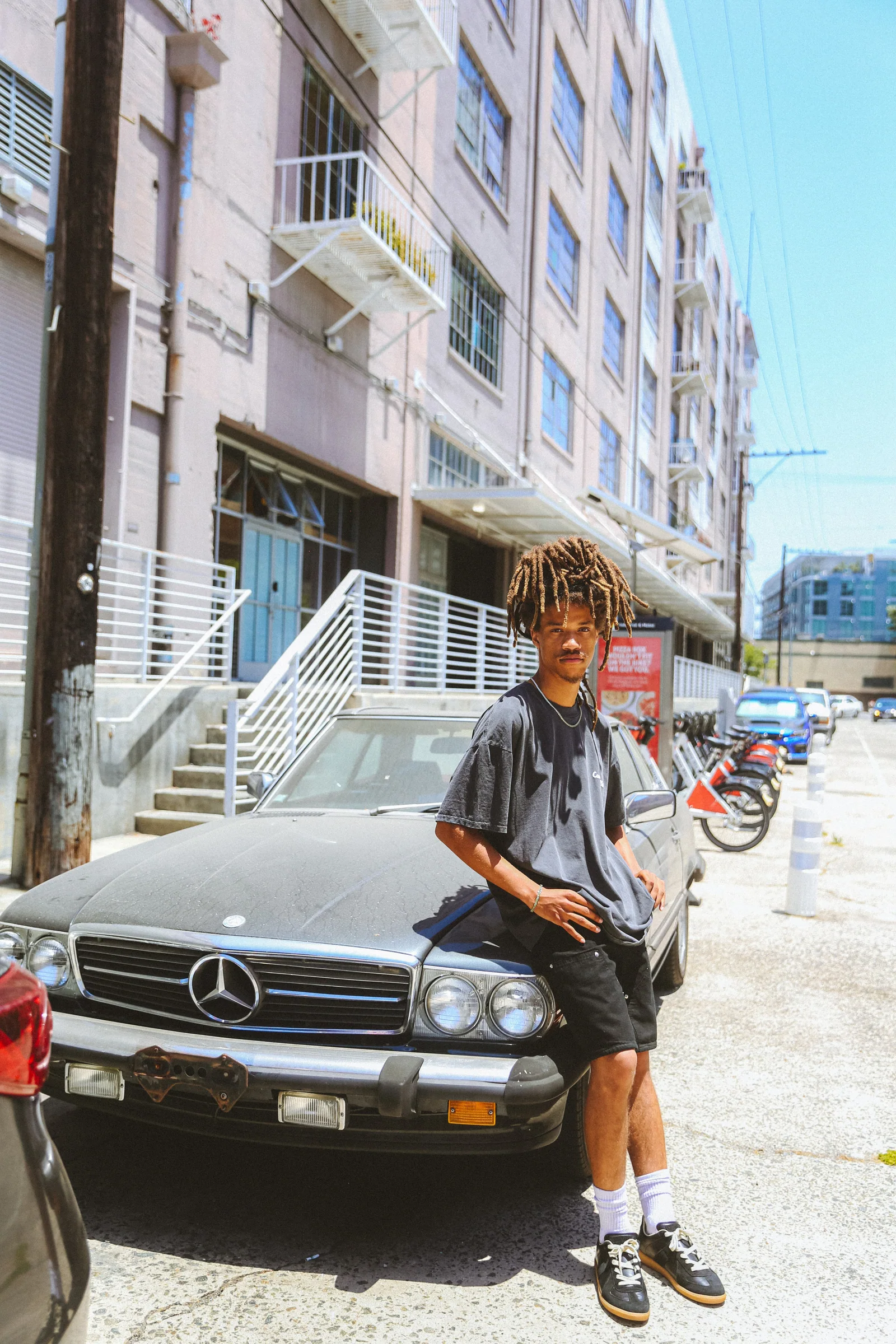 Cannon Mitchel model standing beside a parked car in a bright city street.