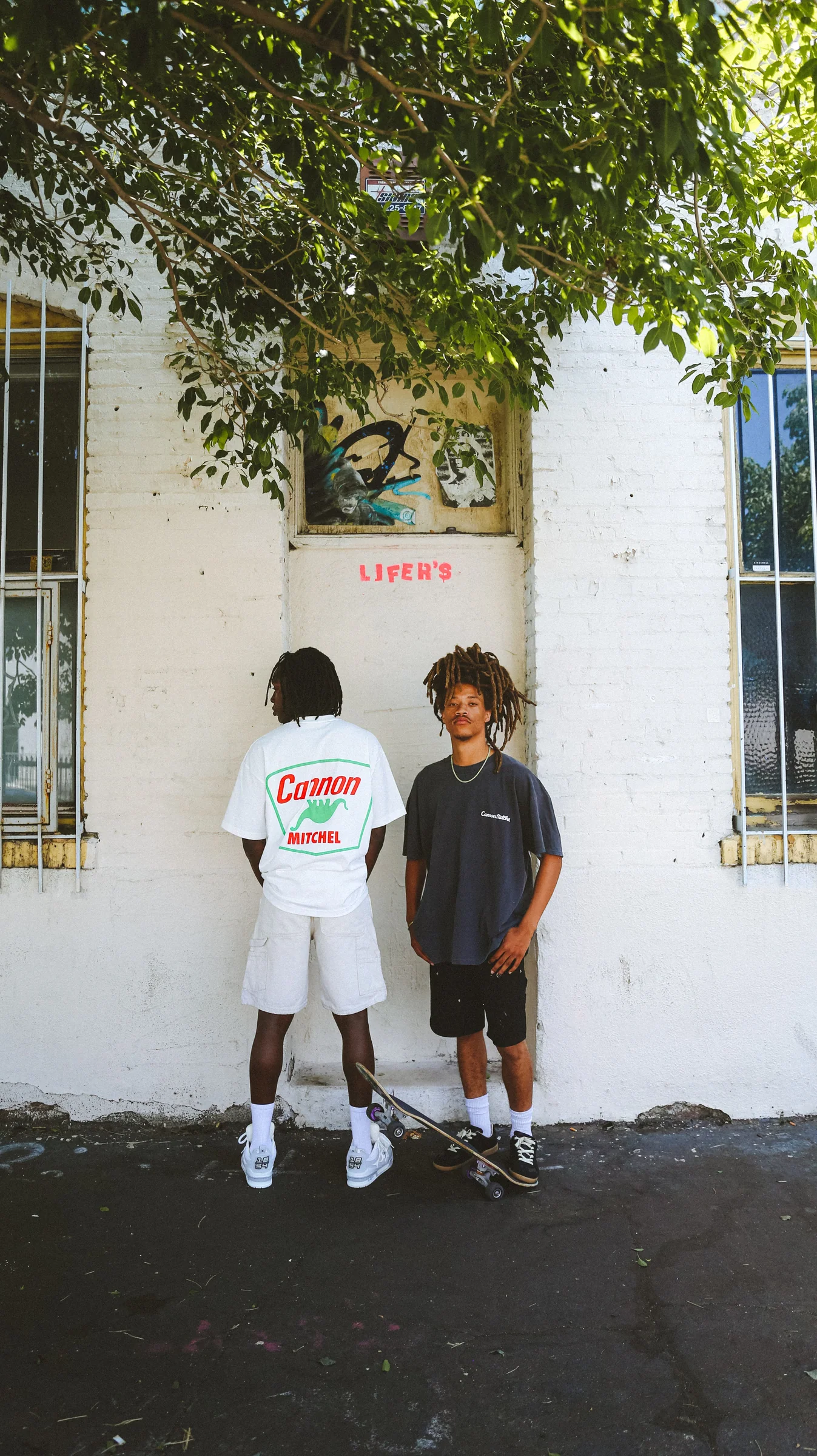 Two Cannon Mitchel models standing against a white wall in summer light.