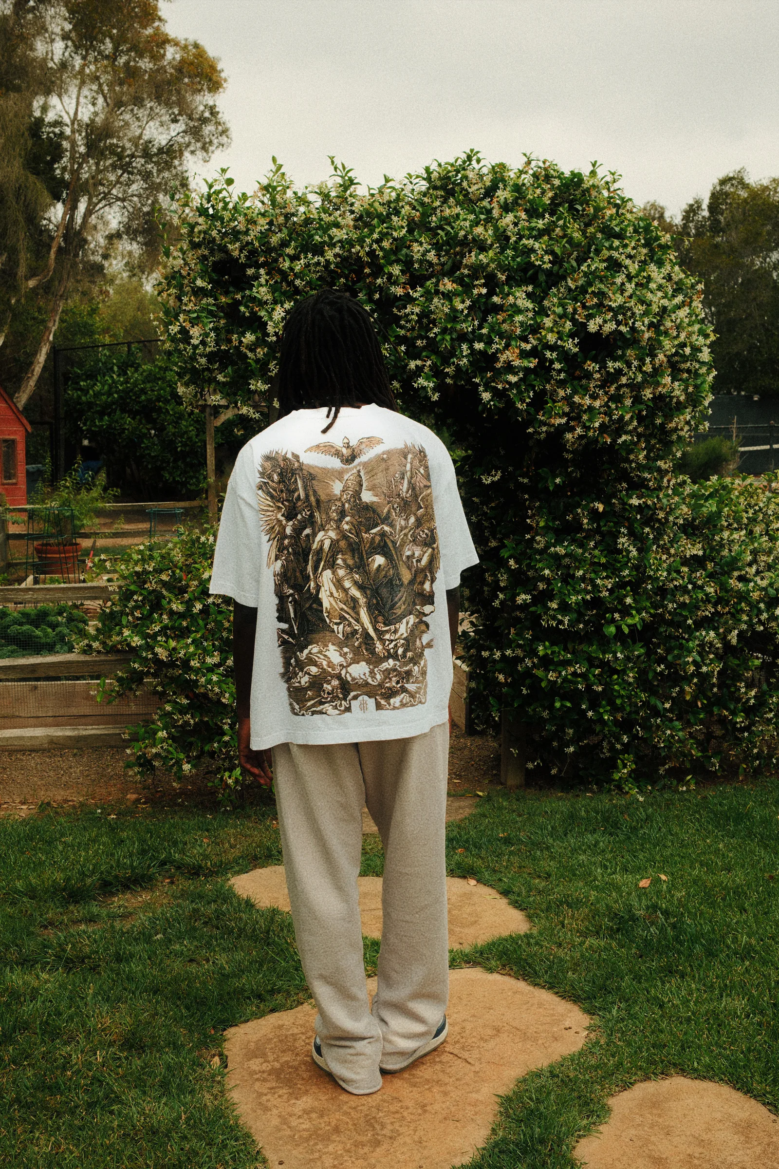 Back view of a white Cannon Mitchel graphic tee in the garden.