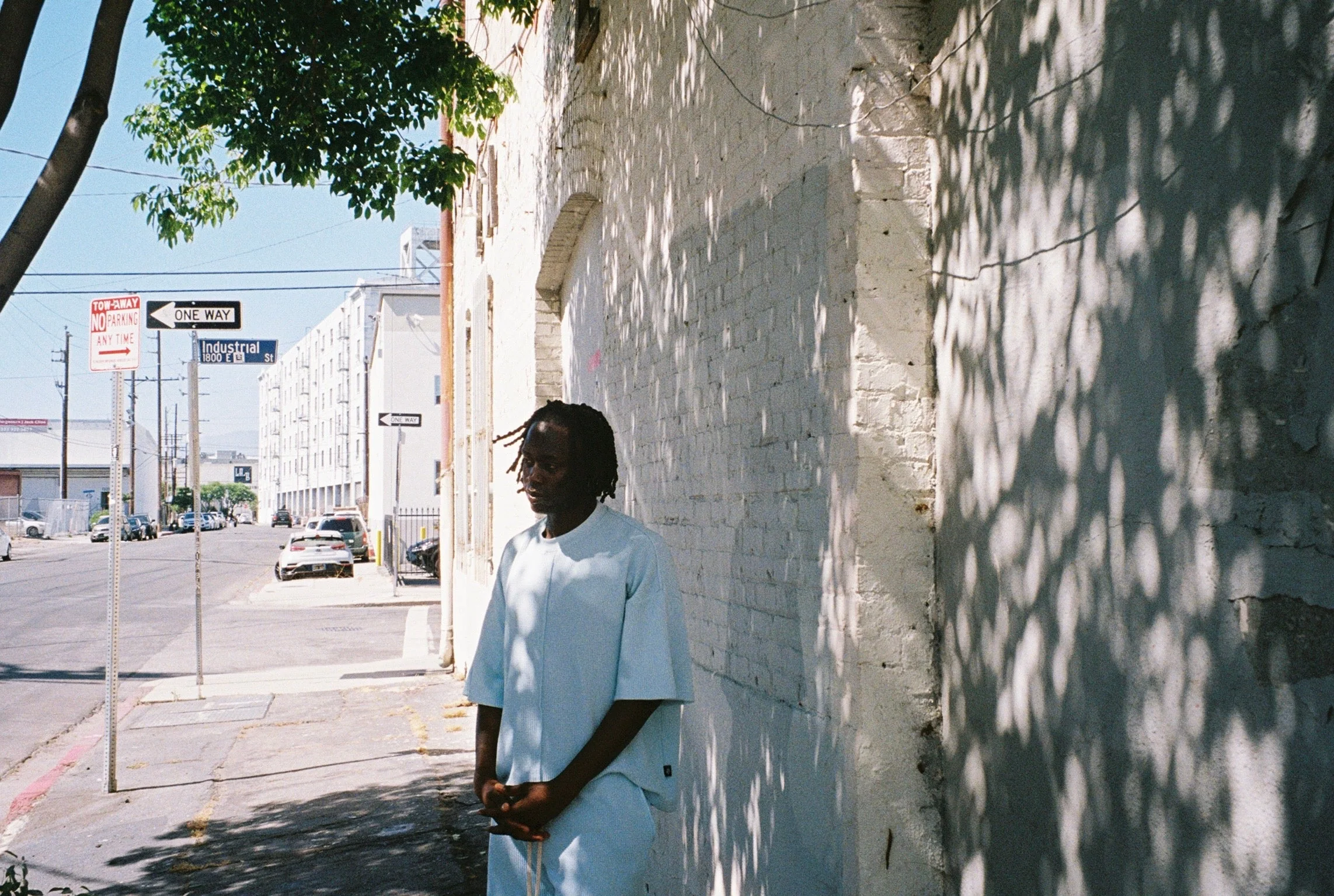 SS26 exterior campaign image with a model standing in wall shadows.