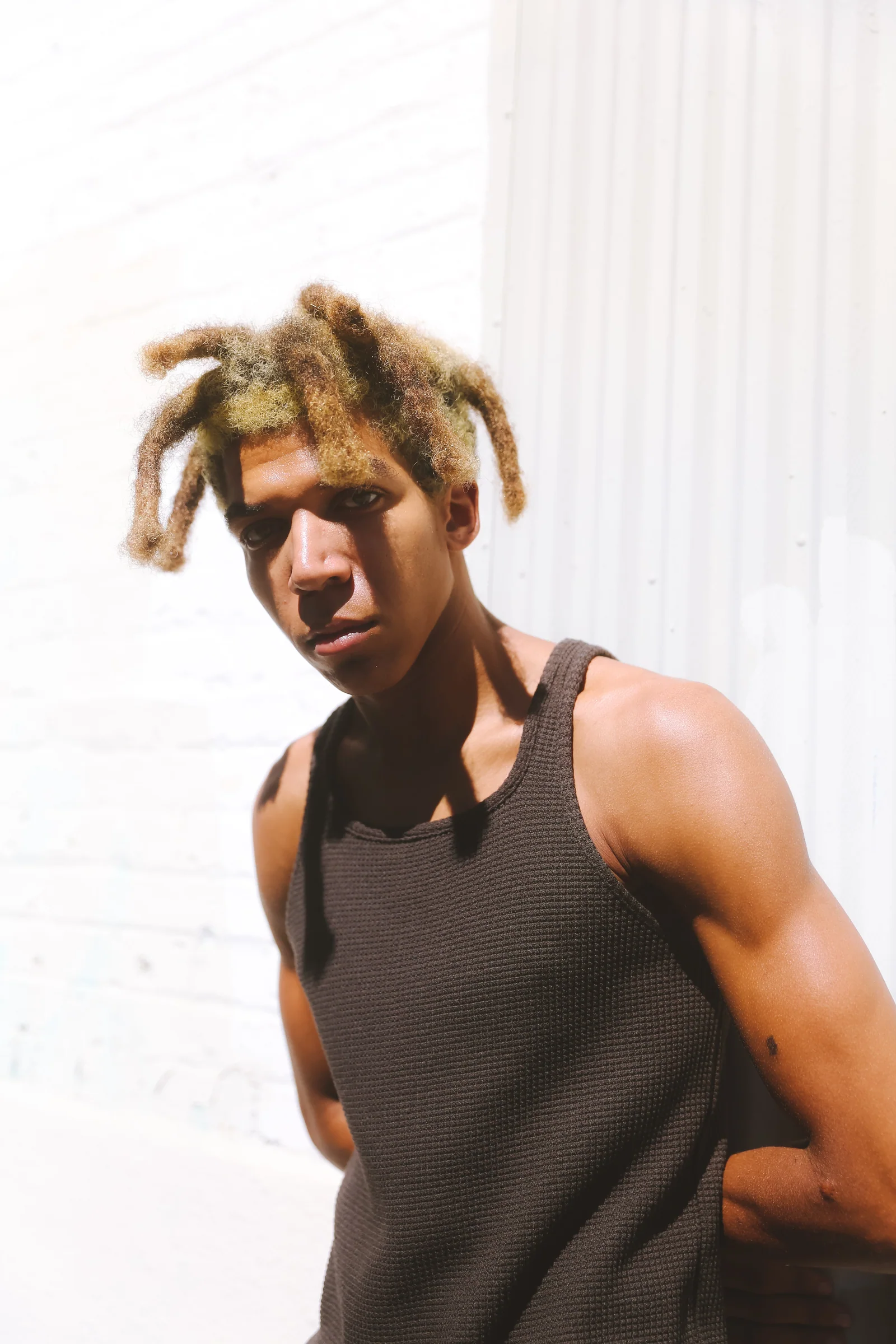 SS26 portrait in a black sleeveless top against a bright exterior wall.
